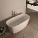 Freistehende Badewanne von Ideal Standard, ovales Design, auf Holzfußboden platziert, mit chromfarbener Armatur und angrenzendem Wandregal.